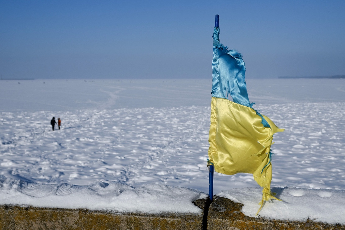 A damaged Ukrainian flag flutters on the embankment as people walk across the frozen Kyiv Reservoir located on the Dnieper north of Kyiv, Ukraine. (AFP)