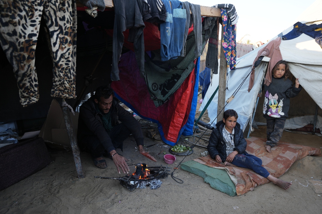 Displaced Palestinian Amr Al-Manaya, 35, sits by the fire with his children, Muhammad and Hala, next to their tent in Deir al-Balah, Gaza Strip. (AP)