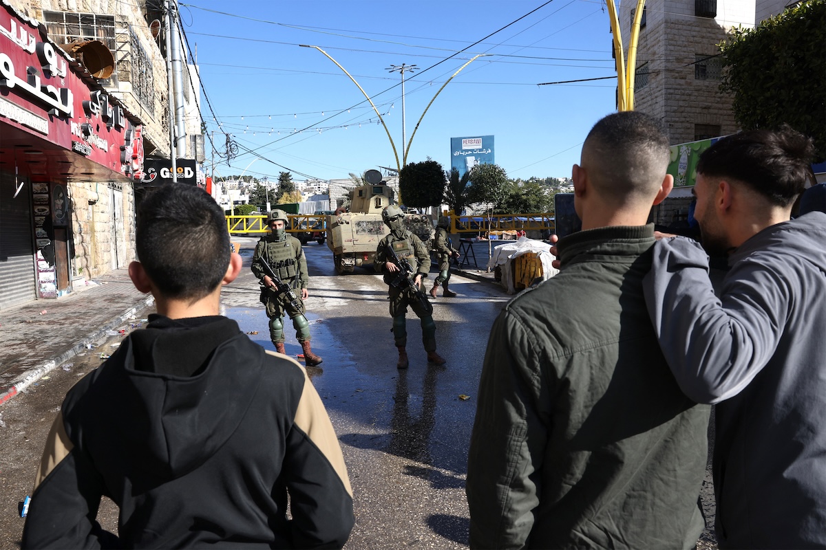 Palestinians watch patrolling Israeli soldiers as the military closes part of the H2 southern sector of the West Bank city of Hebron, announcing a curfew as they search for weapons and Palestinians on their wanted list, in the Israeli occupied West Bank on January 19, 2026. (FILE/AFP)