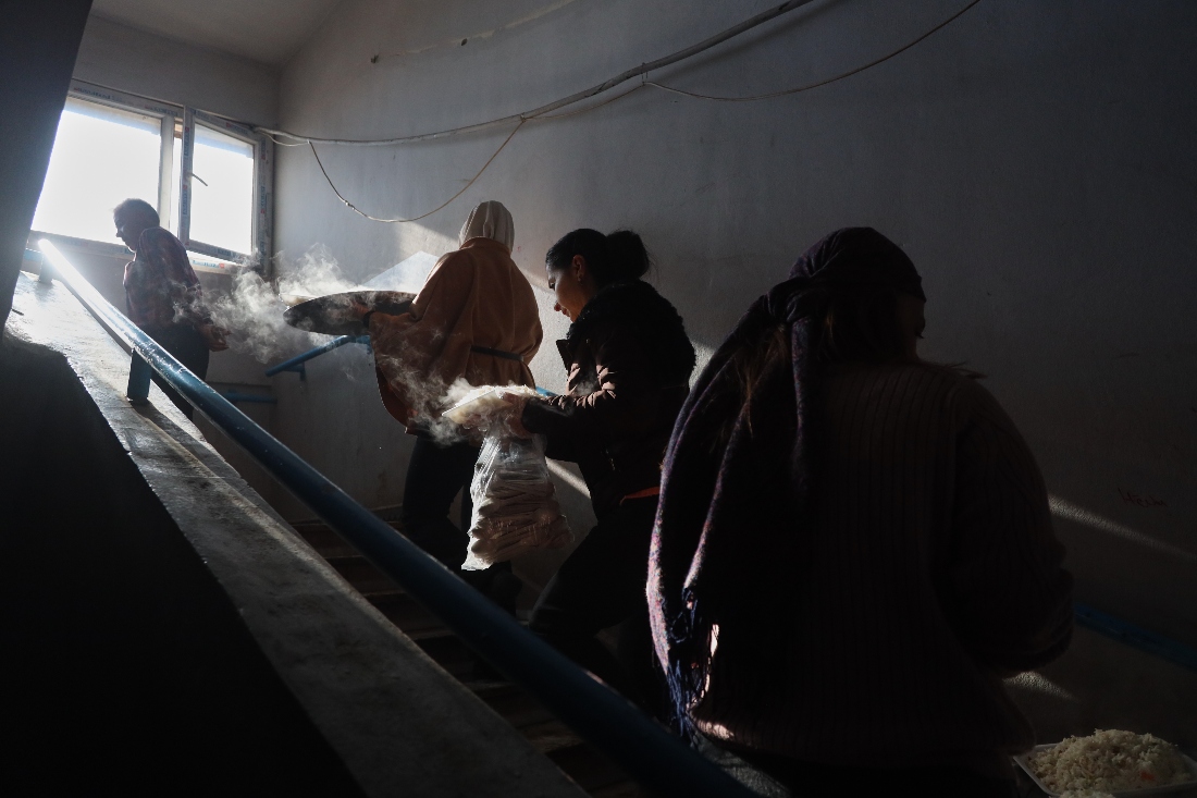 Women carry hot meals upstairs to distribute to displaced families sheltering at a school in Qamishli, northeastern Syria. (AP)