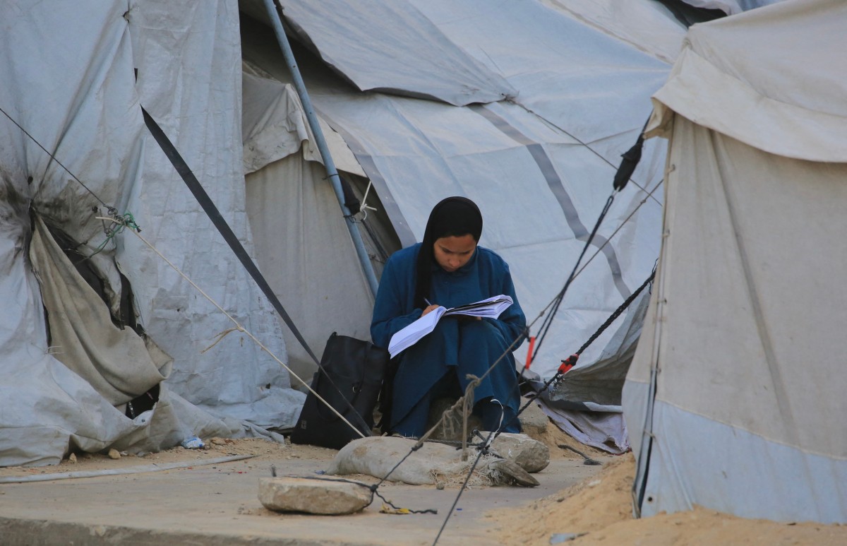 A Palestinian woman writes in a book while seated near tents in Khan Yunis in the southern Gaza Strip, Jan. 27, 2026. (AFP)