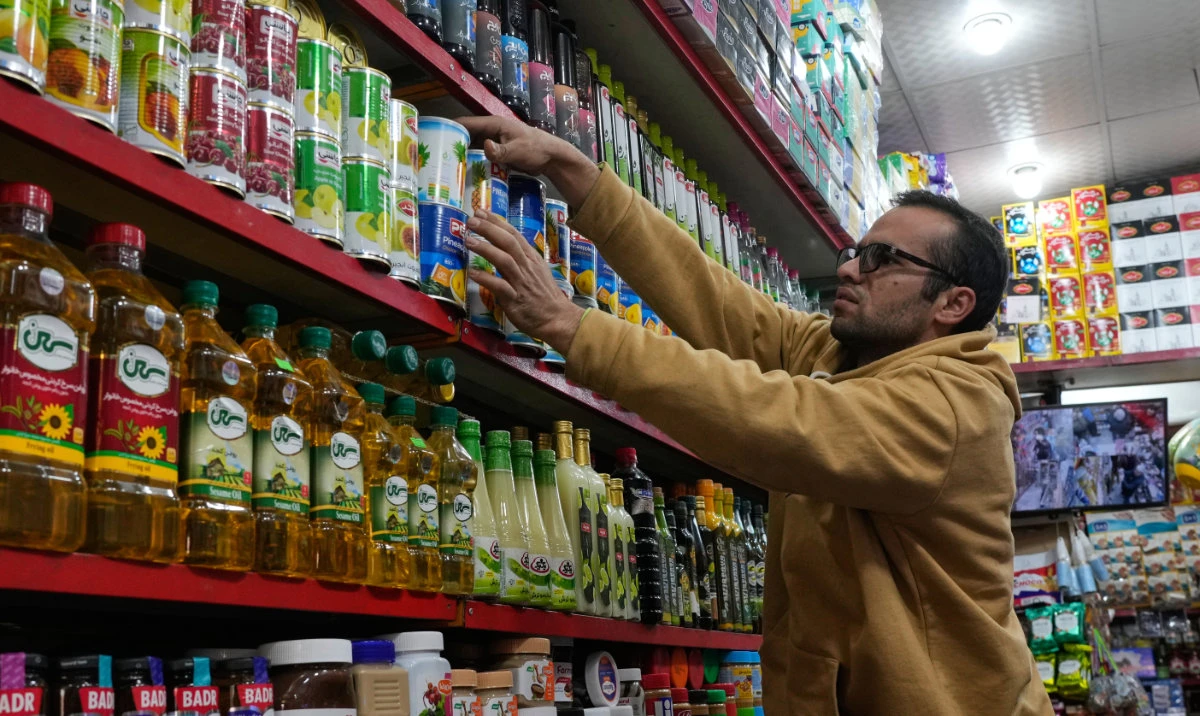 A shopkeeper arranges items on a shelf at his grocery store in northern Tehran, Iran, Tuesday, Jan. 6, 2026. (AP)
