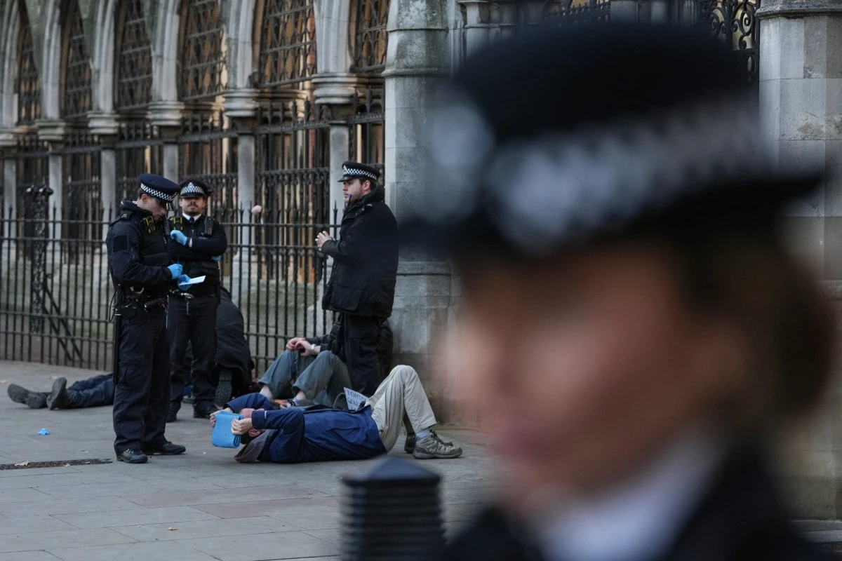 Police stand over protesters (back L-on ground) after they were removed from a demonstration in support of "Defend Our Juries" and their campaign against the ban on Palestine Action, outside the Royal Courts of Justice, Britain's High Court, in central London on November 26, 2025. (AFP)