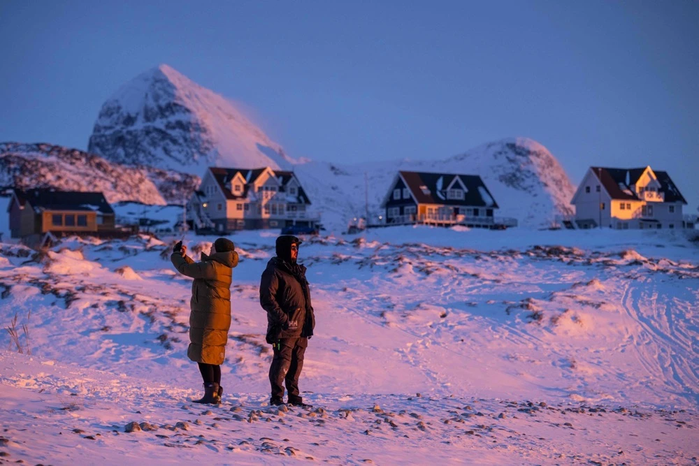 Locals stand on a snowy shoreline at dusk in Nuuk, Greenland. (AFP)