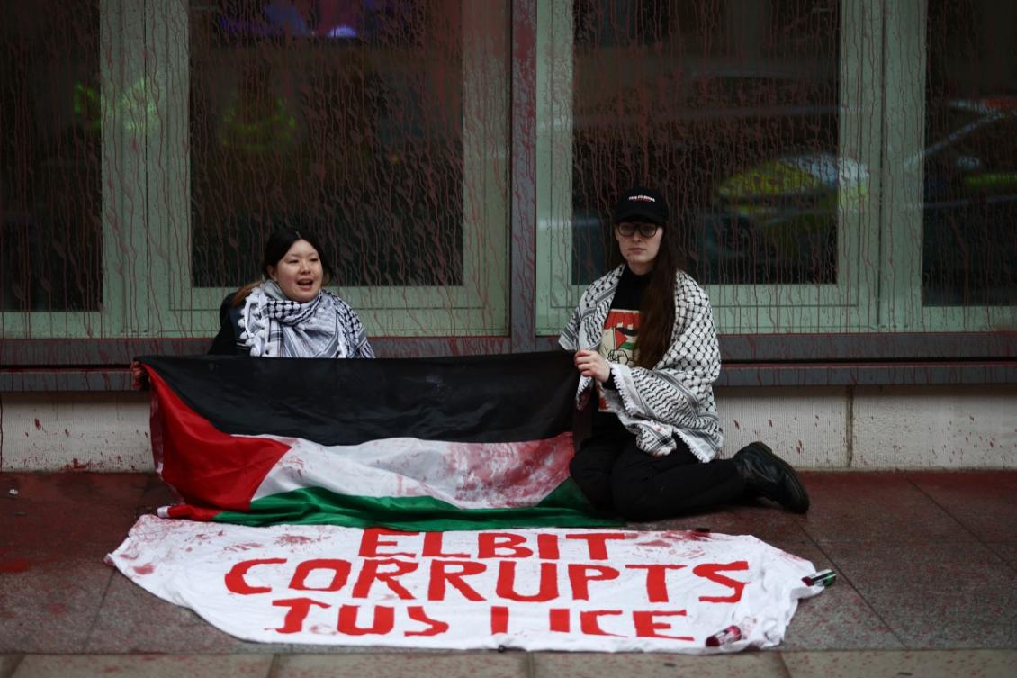 Pro-Palestinian protesters sit on the floor with a sign reading 'Elbit corrupts justice', referring to the Israeli defence group Elbit, after spraying red paint over the exterior of the Ministry of Justice building in central London. (File/AFP)
