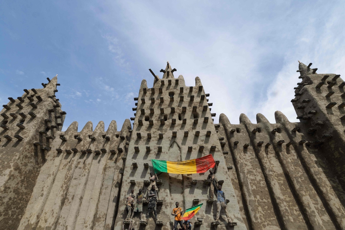 People hold flags of Mali as they climb the walls of the Great Mosque of Djenne during its re-plastering in Djenne, Mali. (AFP)
