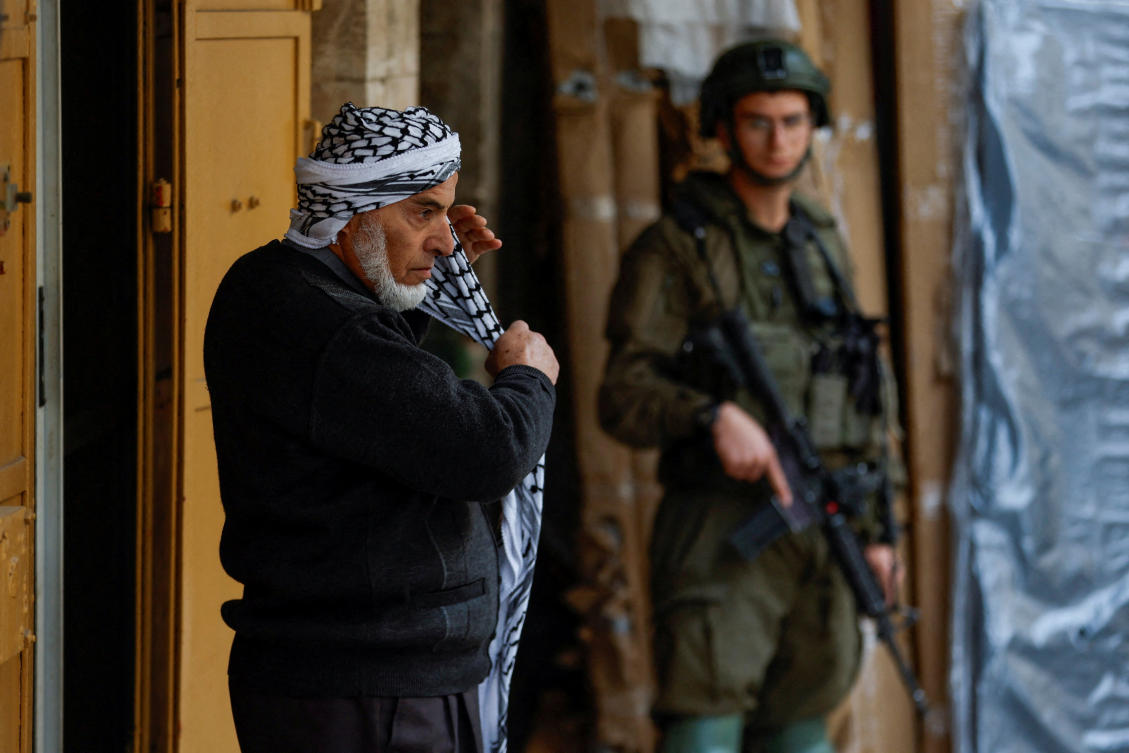 A Palestinian man puts on a keffiyeh as an Israeli soldier stands guard in the old city in Hebron in the Israeli-occupied West Bank on Monday. Israel announced measures to further entrench its control of the territory. (Reuters)
