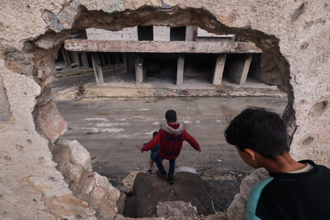 Youths move through a hole in the wall of a damaged school in the Kurdish-majority neighborhood of Sheikh Maqsoud, in Aleppo, Syria. (AP)