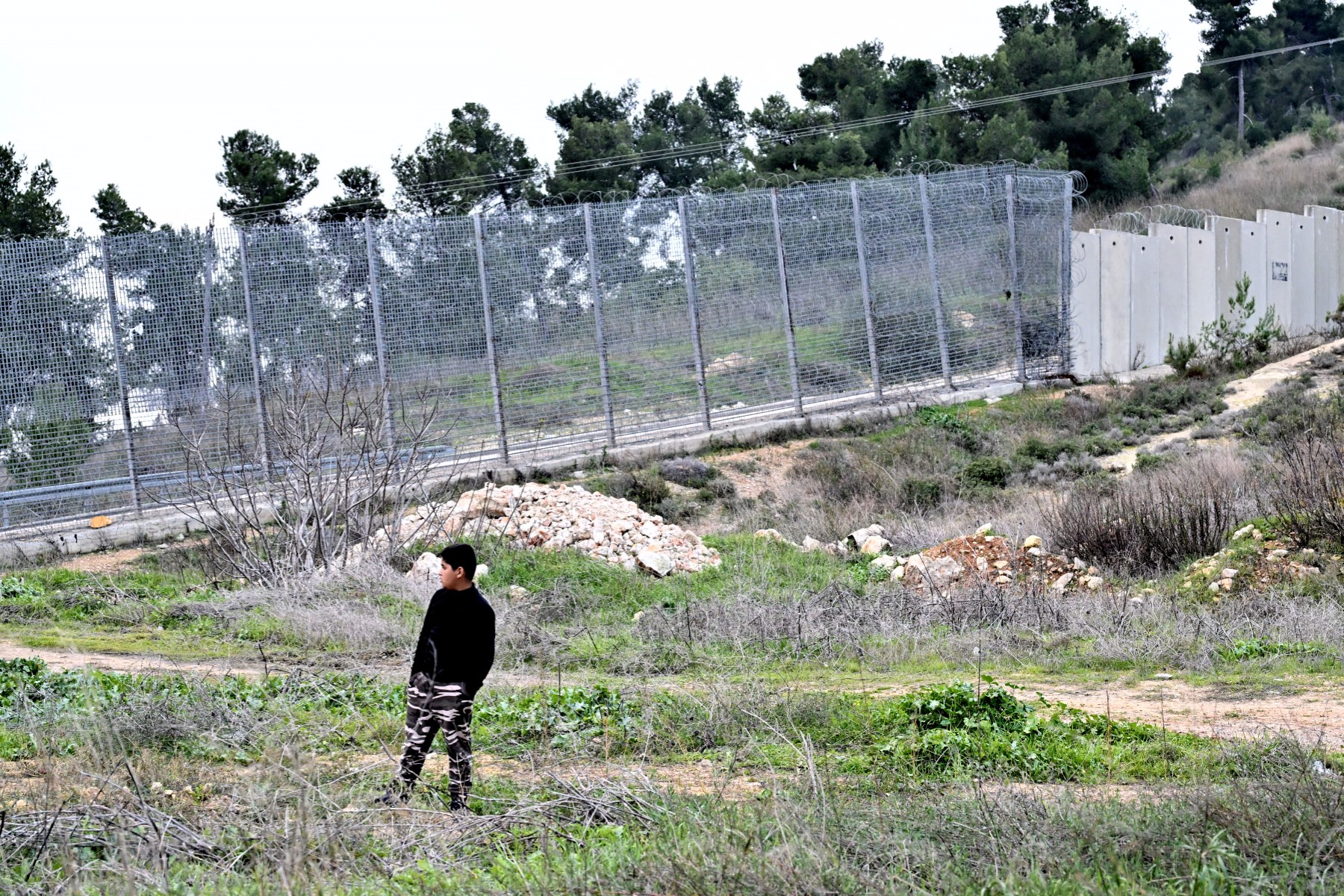 A Palestinian youth stands in a field in front of the West Bank barrier in Al-Walaja, a Palestinian village in annexed East Jerusalem on December 28, 2023. (AFP)