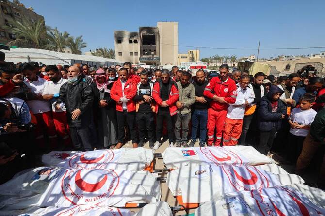 Members of the Palestine Red Crescent and other emergency services pray by the bodies of fellow rescuers killed by Israeli forces in March last year. (AFP/File)