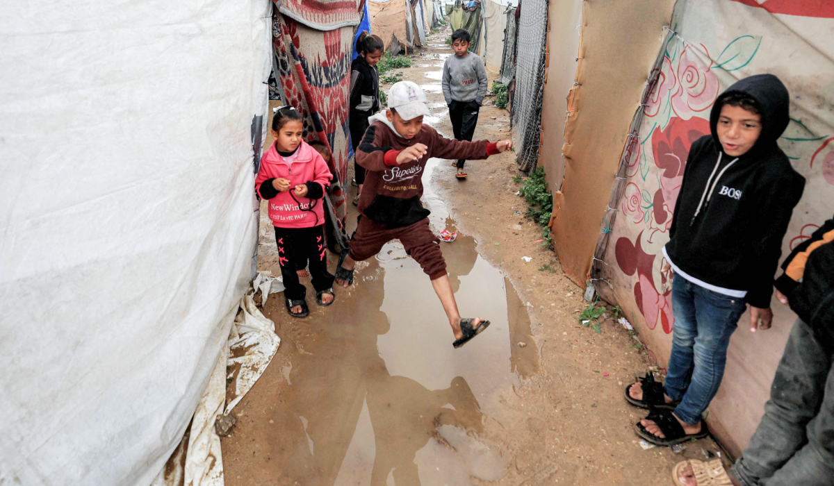 A boy jumps across a water puddle between tents sheltering people displaced by war at the Bureij camp for Palestinian refugees in the central Gaza Strip on February 24, 2026. (AFP)