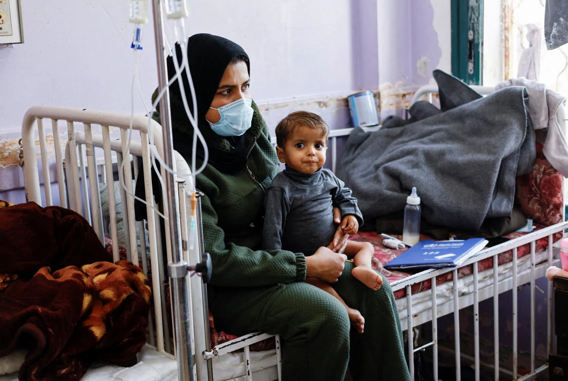 Dena Abu Youssef, sister of Mahmoud Abu Youssef, a Palestinian boy who is receiving treatment at Al-Aqsa Martyrs Hospital, holds him as she sits on a hospital bed, in Deir Al-Balah, central Gaza Strip, February 2, 2026. (Reuters)