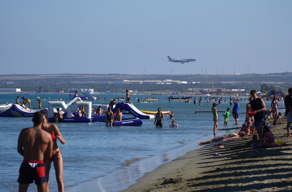 People walk on the beach at Lady's Mile in the Cypriot port city of Limassol as a Voyager A330 lands at nearby Royal Air Force (RAF) Akrotiri base, in a British Sovereign Base Area in the southern region of Cyprus, on August 17, 2022. (FILE/AFP)