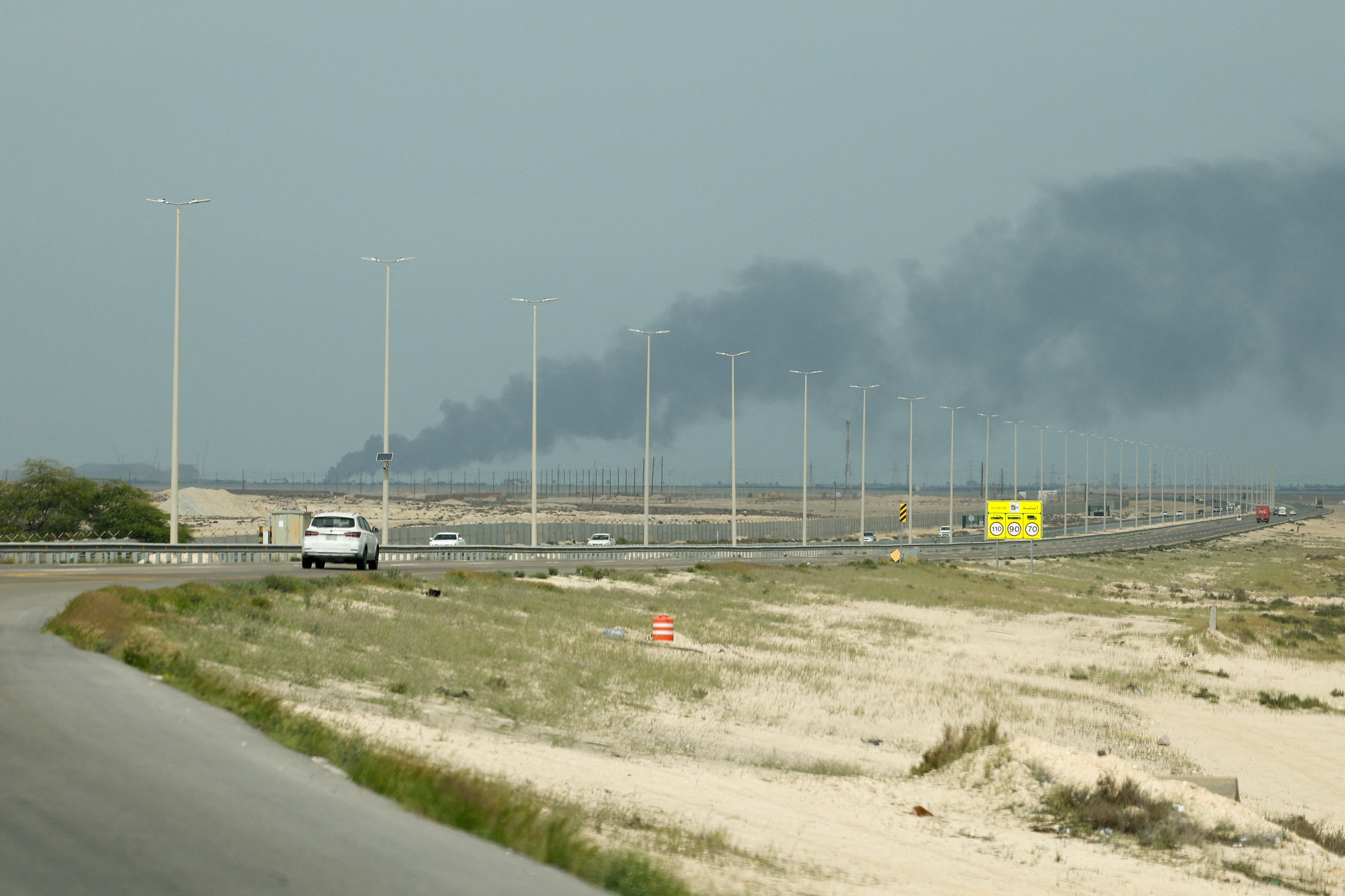Vehicles move along a road as smoke billows from Saudi Aramco's Ras Tanura oil refinery. (Reuters)