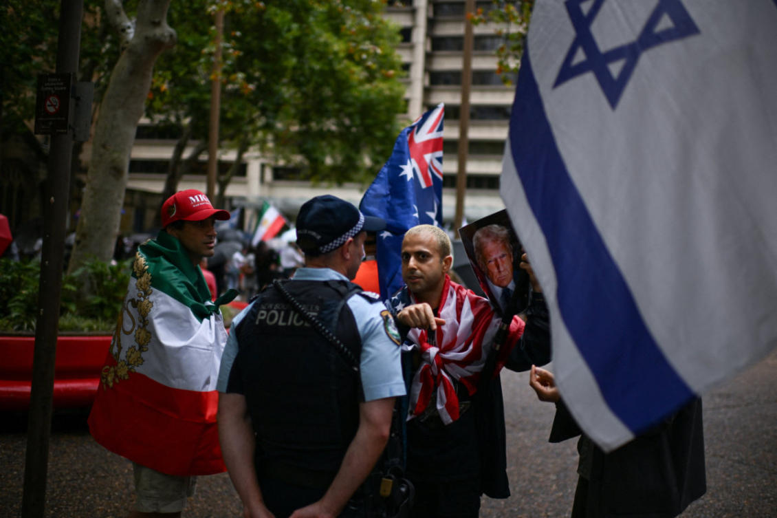 A man holding an image of US President Donald Trump speaks with a police officer during a rally in support of political change in Iran at Town Hall Square in Sydney, Australia, on March 8, 2026. (REUTERS)