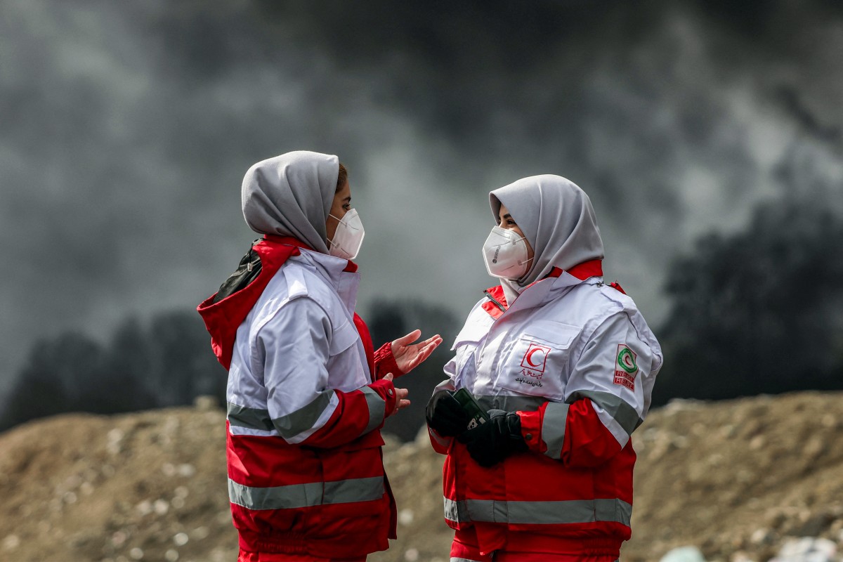Women members of Iran’s Red Crescent society stand near smoke plumes from an ongoing fire following an overnight airstrike on the Shahran oil refinery in northwestern Tehran, March 8, 2026. (AFP)