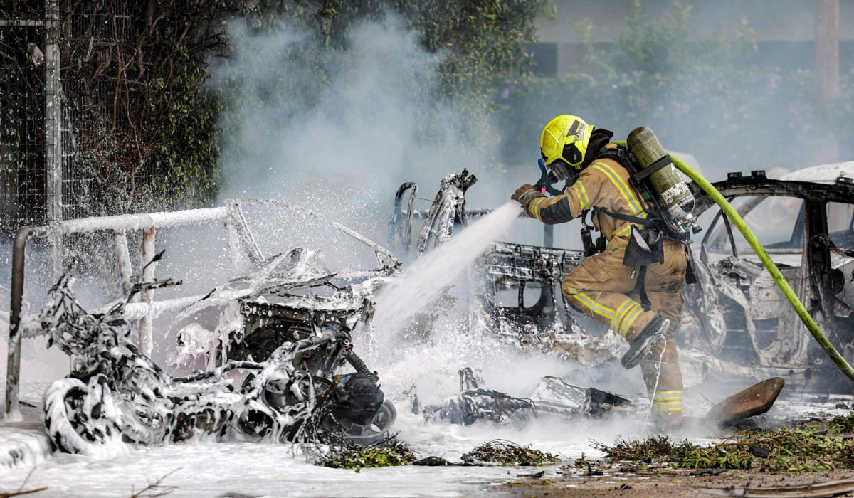 A firefighter extinguishes a blaze in a vehicle following a projectile impact from an Iranian strike in southern Tel Aviv on March 15, 2026. (AFP)