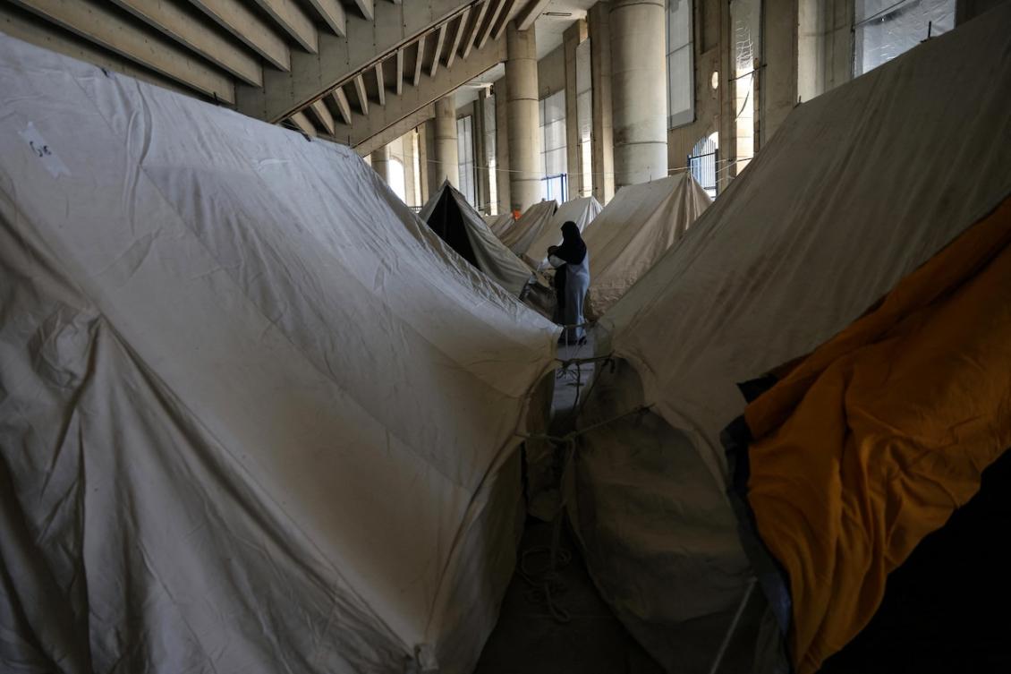 A displaced woman walks between tents inside the Camille Chamoun Sports City stadium, which was converted into a reception and shelter facility for displaced people, in Beirut on March 10, 2026. (FILE/AFP)