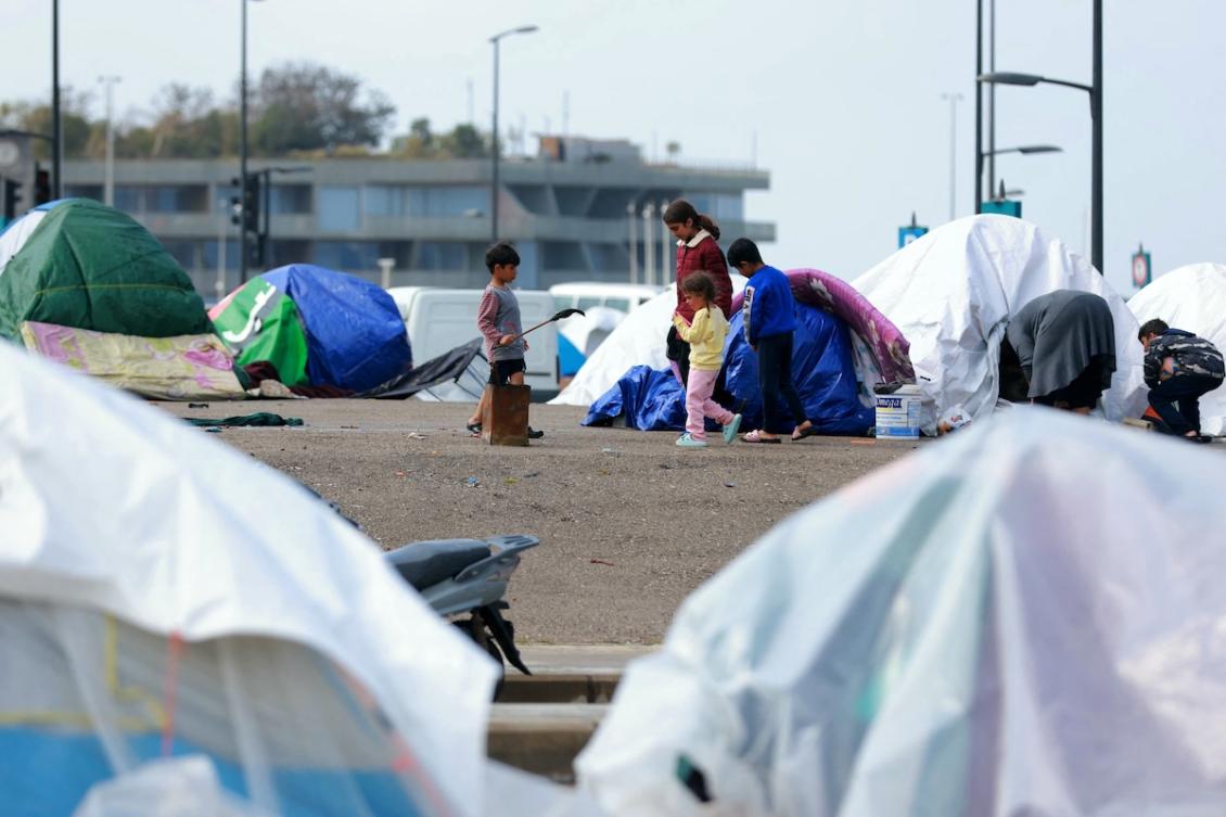 Displaced family members stand outside their tent covered in plastic sheeting to shield them from the stormy weather along Beirut’s seafront area on March 15, 2026. (FILE/AFP)