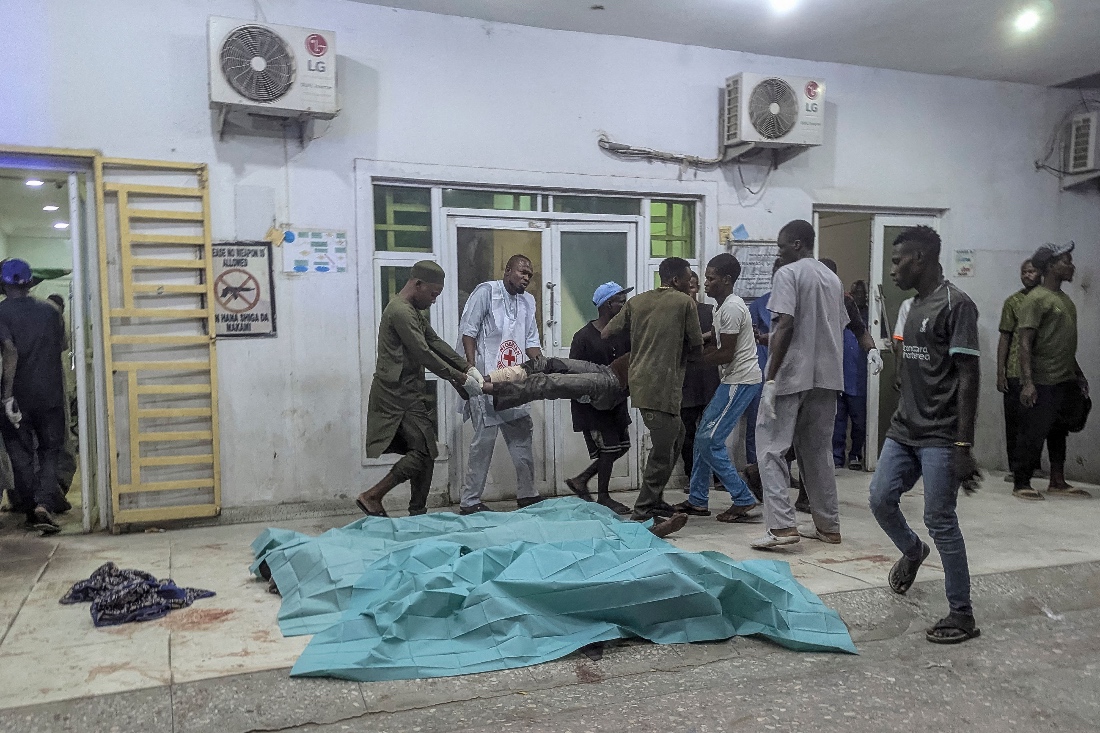 People carry an injured man past bodies covered with sheets at a hospital in Maiduguri following blasts in the city, Nigeria. (AFP)