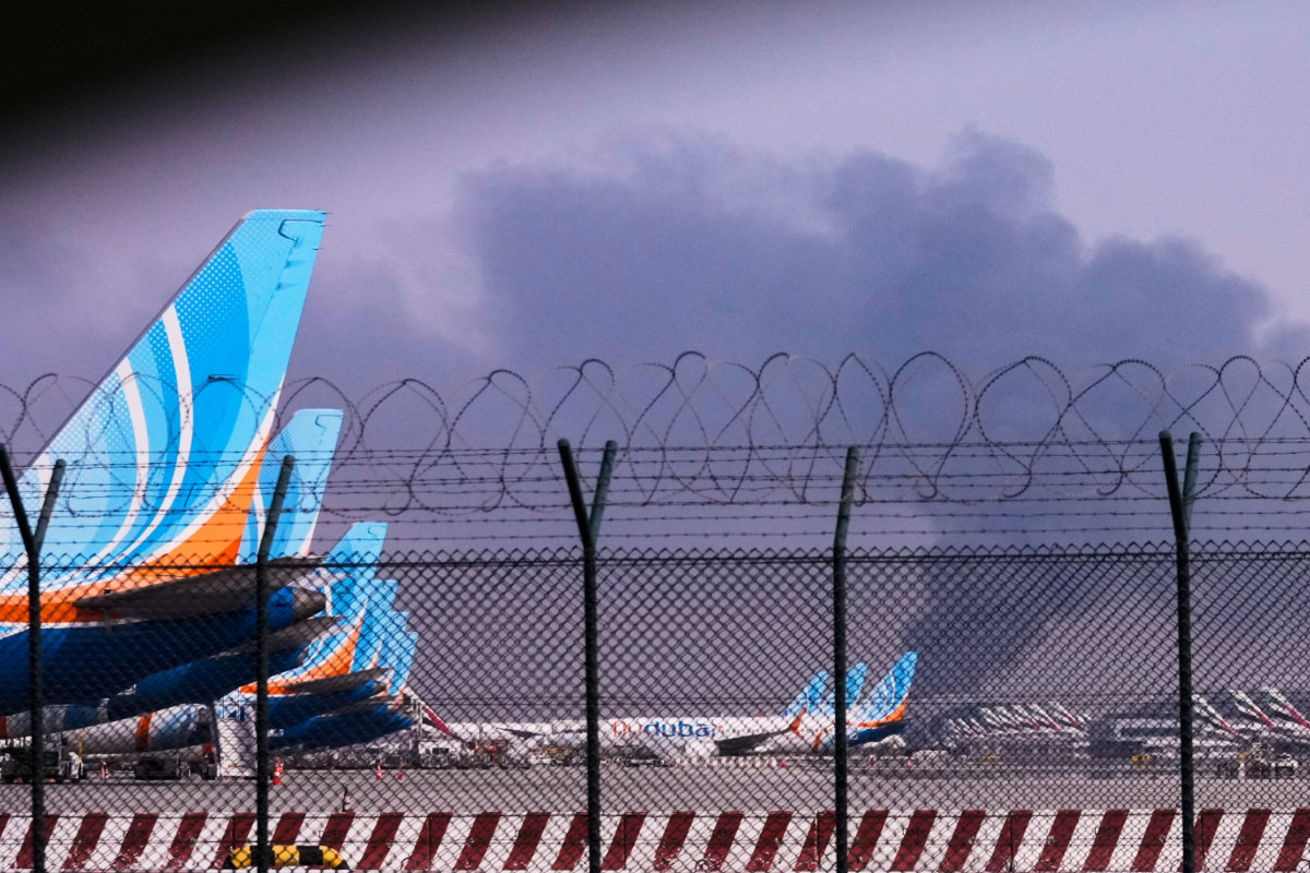 FlyDubai planes parked at Dubai International Airport as smoke rises in the background after a drone struck a fuel tank early morning, forcing the temporary suspension of flights, in Dubai, on March 16, 2026. (AP Photo)