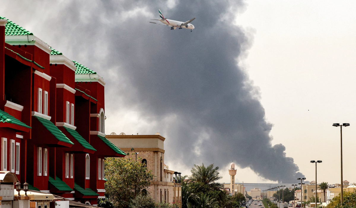 An Emirates aircraft prepares for landing as a smoke plume rises from an ongoing fire near Dubai International Airport in Dubai on March 16, 2026. (AFP)