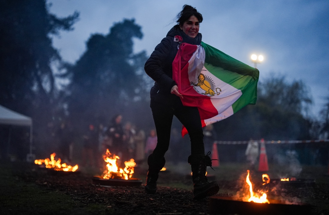 A woman carrying Iran's historic "Lion and Sun" flag leaps over fire during the Nowruz Fire Festival marking the Persian New Year, in West Vancouver, British Columbia. (AP)