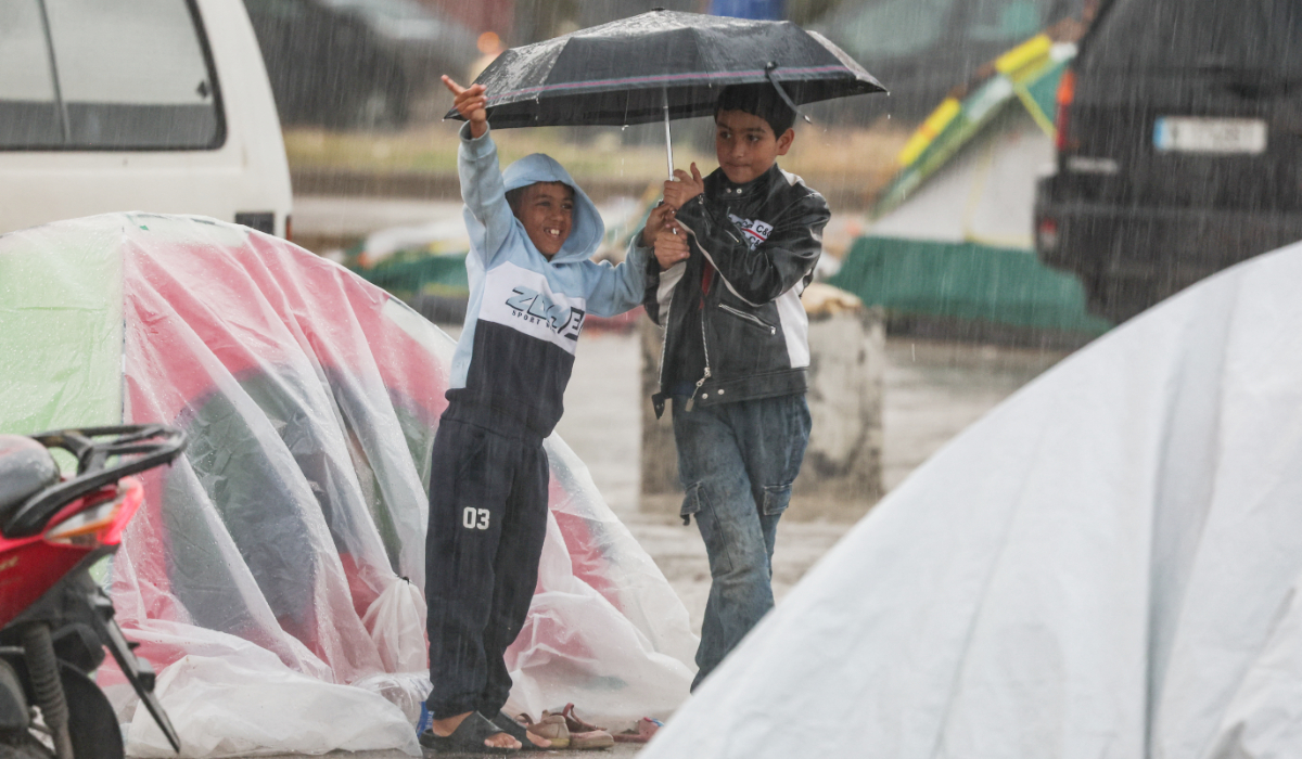 Children take shelter from the rain on Saturday as they stand next to tents used by displaced people, during Eid Al-Fitr celebrations, in Beirut. (Reuters)