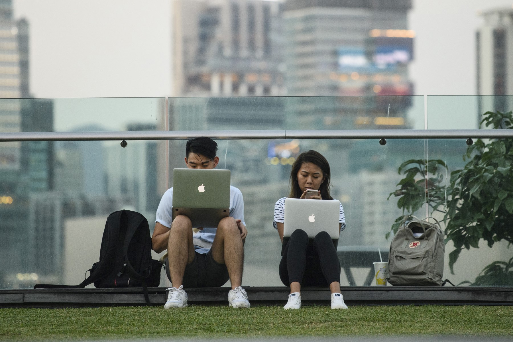A man and woman use their laptops and a mobile phone as they sit in a park next to Victoria Harbour in Hong Kong. (AFP)