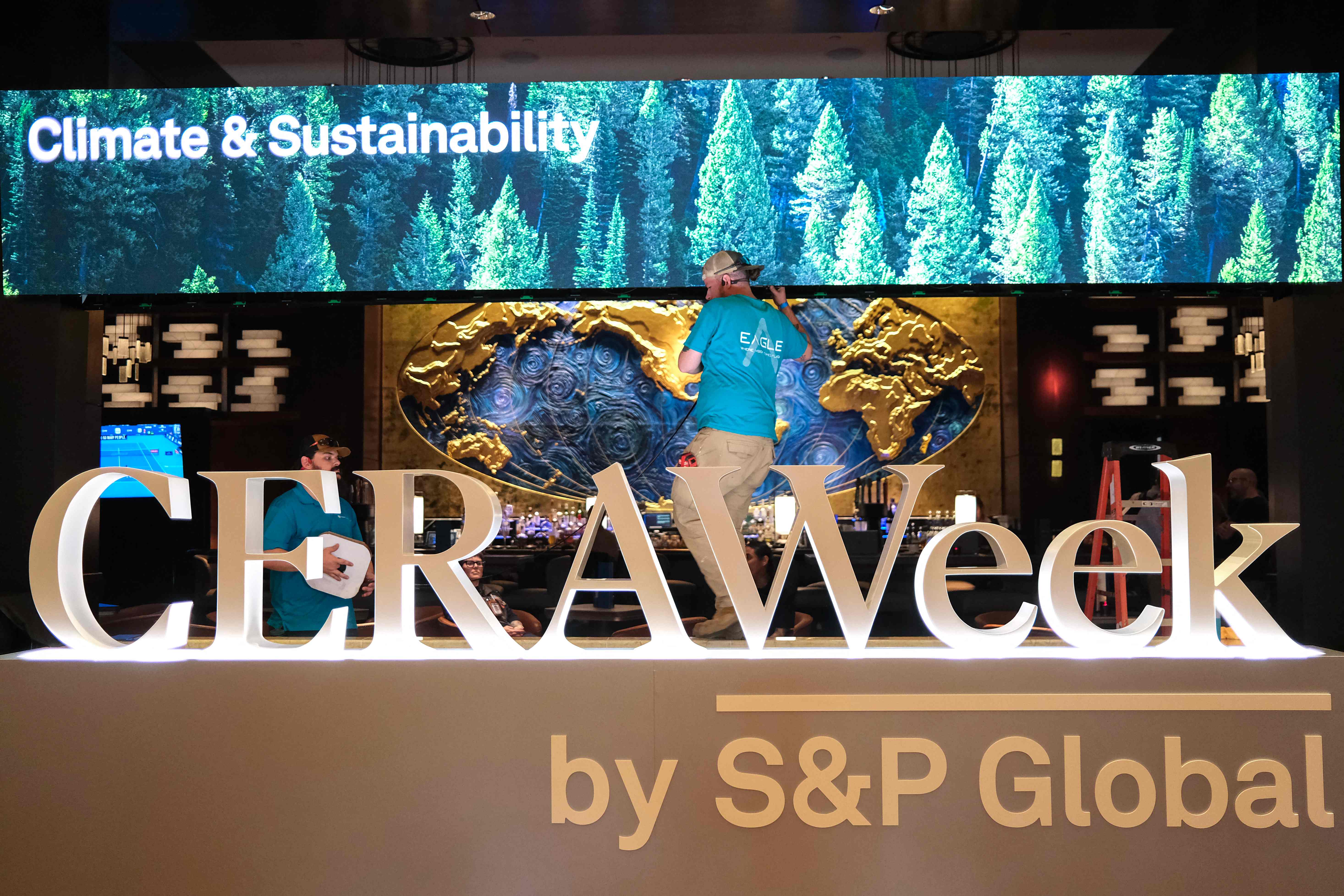 Two men work next to a sign of CERAWeek in Houston, Texas, on March 22, 2026. CERAWeek by S&P Global, an annual conference for the energy industry, begins March 23. Ronaldo Schemidt/AFP