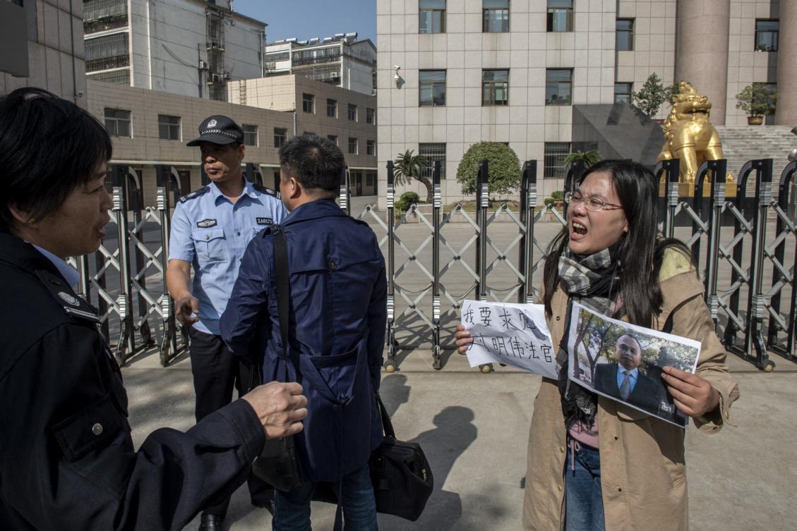This photo taken on October 31, 2019 shows Xu Yan (R), wife of human rights lawyer Yu Wensheng, holding a piece of paper the reads "I want to request a meeting with Judge Liu Mingwei" and a picture of her husband as she stands next to one of her lawyers Xie Yang (C-in dark blue) as security personnel (L) ask them to move away outside the Xuzhou Intermediate People’s Court in Xuzhou. (File/AFP)