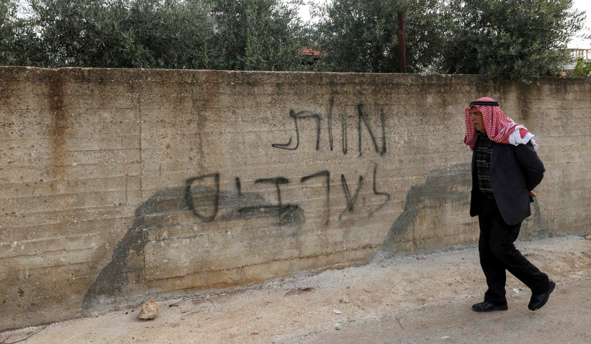 A Palestinian man walks past Hebrew graffiti that reads, 'Death to Arabs', on the wall of a home damaged house in a reported attack by Israeli settlers in the village of Deir al-Hatab, east of the city of Nablus, in the Israeli-occupied West Bank on March 23, 2026. (AFP)