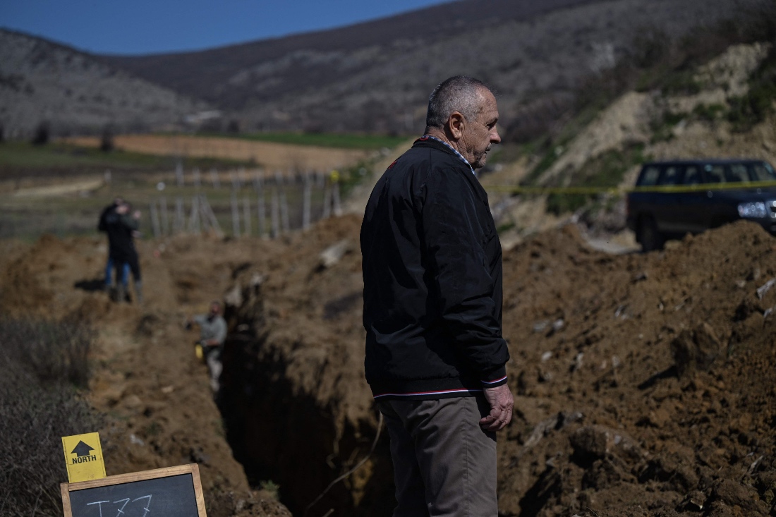 Relative of a missing person Halit Krendali stands over the edge of a freshly dug hole as forensic experts measure a freshly dug hole during excavations near the town of Rahovec, Kosovo. (AFP)