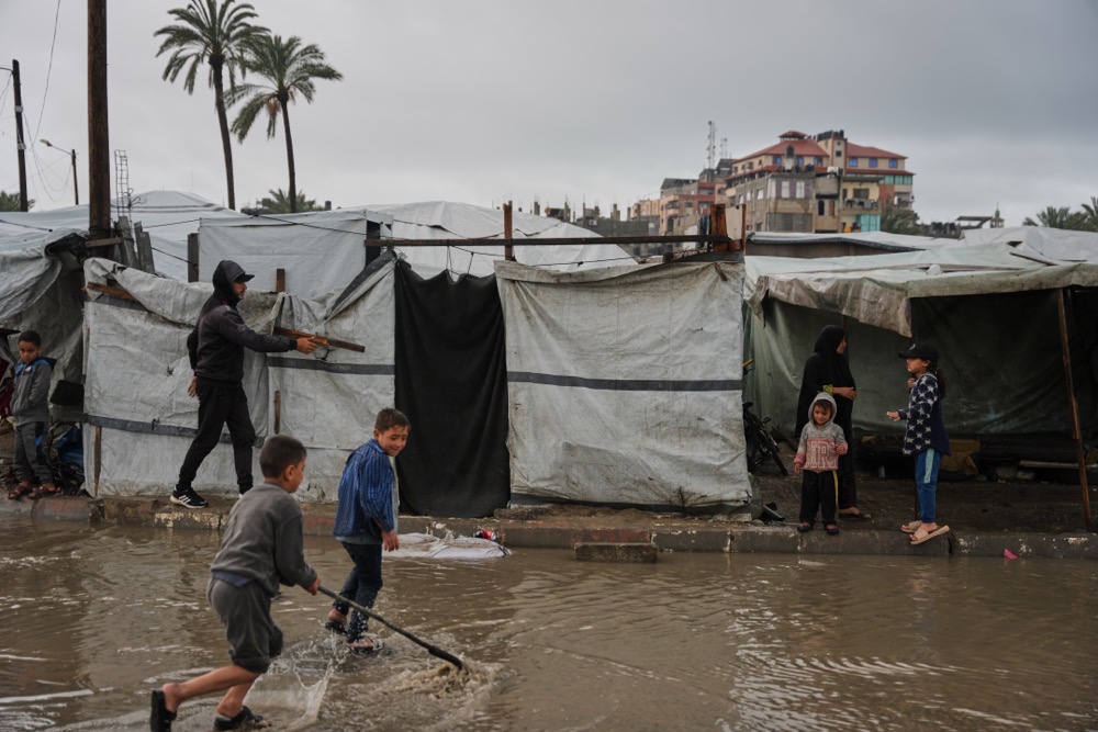 Displaced Palestinian children walk through a rain-soaked tent camp on Thursday, following heavy rainfall in Deir Al-Balah, central Gaza Strip. (AP)