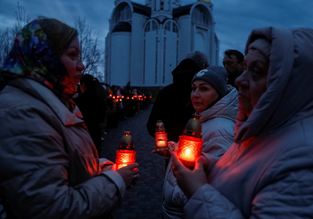 People bring candles to pay tribute at the memorial installation for the victims of attacks and executions by Russian troops in Bucha, Ukraine. (Reuters)