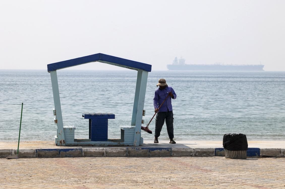 A picture taken on April 29, 2023, shows a municipal worker sweeping a seaside promenade as a shipping vessel sails past Iran's Gulf island of Qeshm. (FILE/AFP)