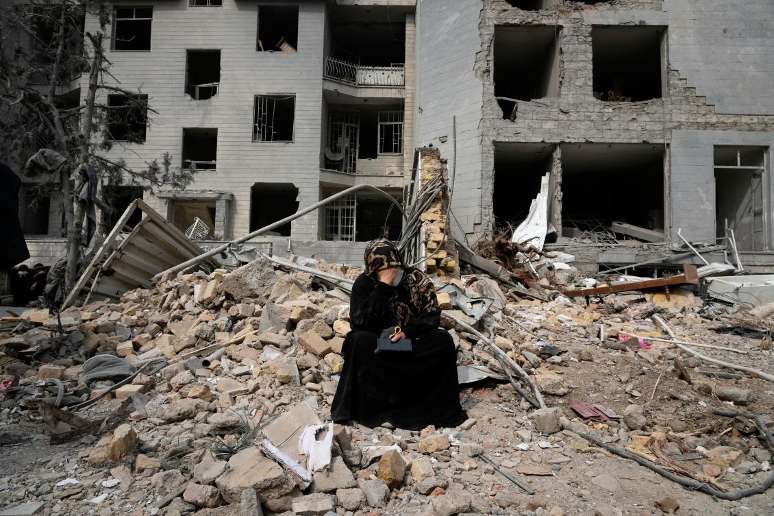 A woman sits on rubble across from a residential building damaged last Sunday during the U.S.-Israeli air campaign in Tehran, Iran, March 12, 2026. (AP)