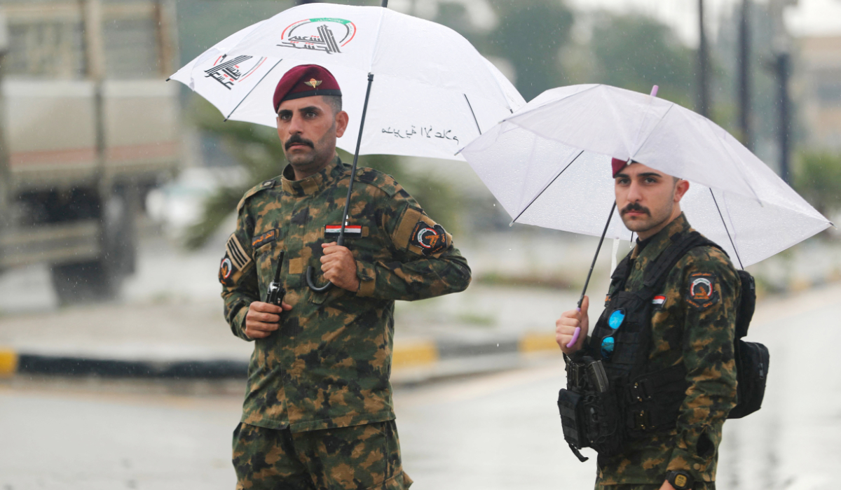Members of Iraqís Hashed al-Shaabi, an alliance of factions now integrated into the regular army, stand under umbrellas as they guard the streets during the funeral for members of the Hashed al-Shaabi Forces in Baghdad on March 24, 2026. (AFP)