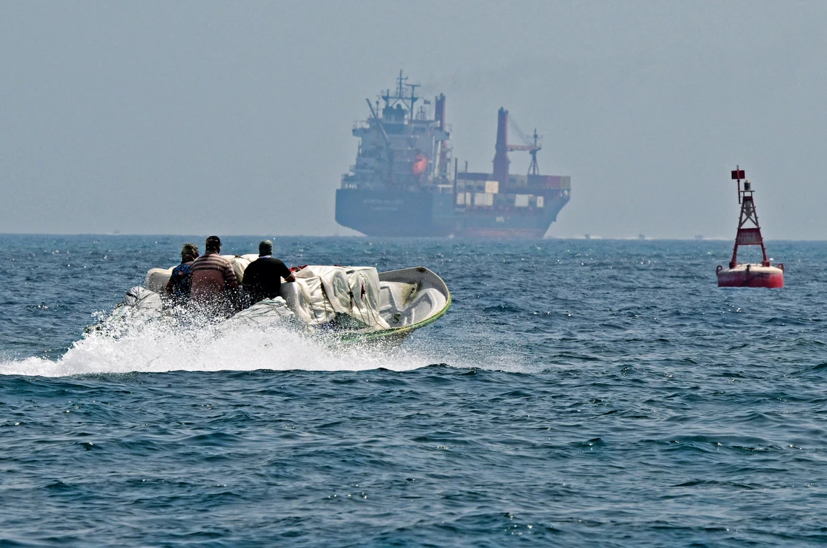 A small boat loaded with merchandise sails a container ship in the waters of the Strait of Hormuz off the coast of Khasab in Oman on June 25, 2025. In 2024, Saudi Arabia alone moved 5.5 million barrels of oil per day through the waterway. (AFP)