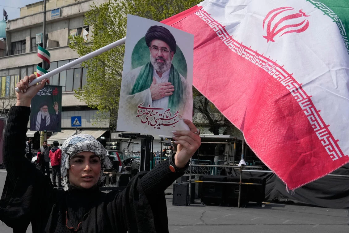 A woman displays a poster of the Iranian Supreme Leader Ayatollah Mojtaba Khamenei as she waves her country’s flag during a campaign in support of the government at the Enqelab-e-Eslami, or Islamic Revolution, square in downtown Tehran, Mar. 14, 2026. (AP)