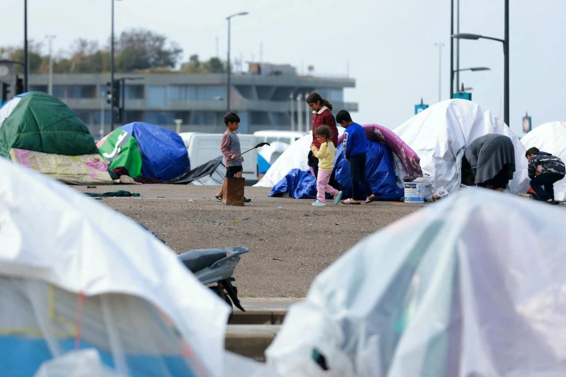 Displaced family members stand outside their tent covered in plastic sheeting to shield them from the stormy weather along Beirut’s seafront area on March 15, 2026. (FILE/AFP)