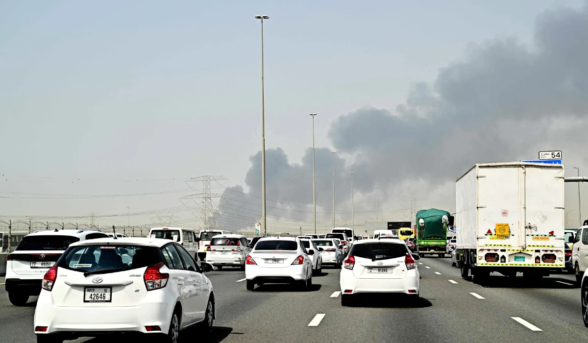 Smoke billows from an ongoing fire near Dubai International Airport as vehicles drive on a highway in Dubai on March 16, 2026. (AFP)