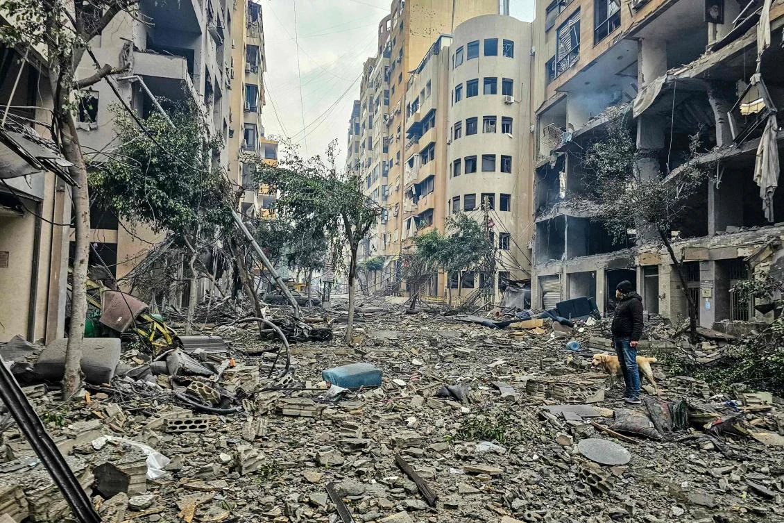 A man and his dog walk across the rubble of a building at the site of an Israeli airstrike in Beirut’s southern suburb Haret Hreik on Mar. 15, 2026. (AFP)