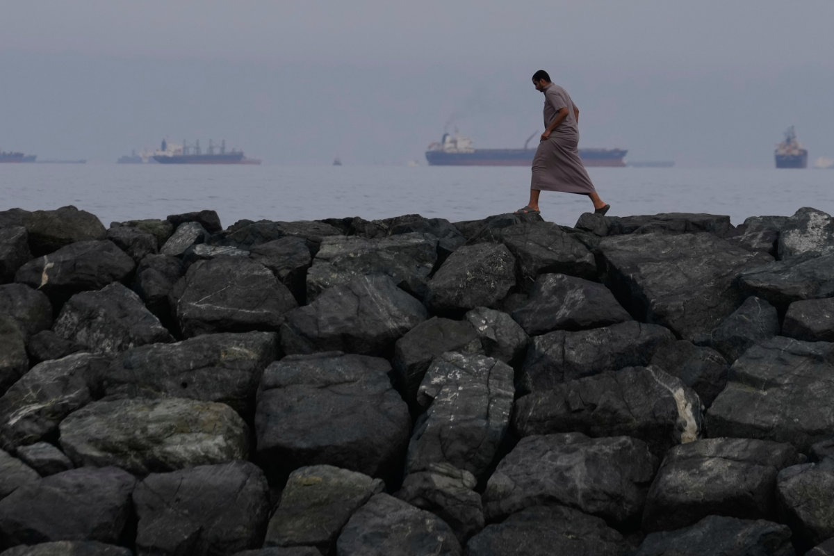 A man walks along the shore as oil tankers and cargo ships line up in the Strait of Hormuz on March 11, 2026, seen from Khor Fakkan, UAE. (AP Photo)