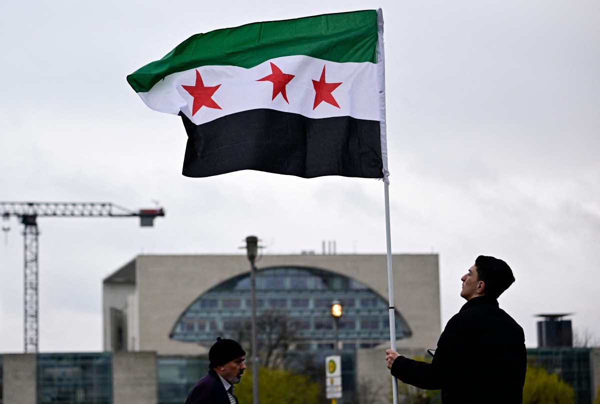 Demonstrators wave the Syrian flag in front of the Chancellery (background) before the meeting between the German chancellor and the Syrian president in Berlin. (File / AFP)