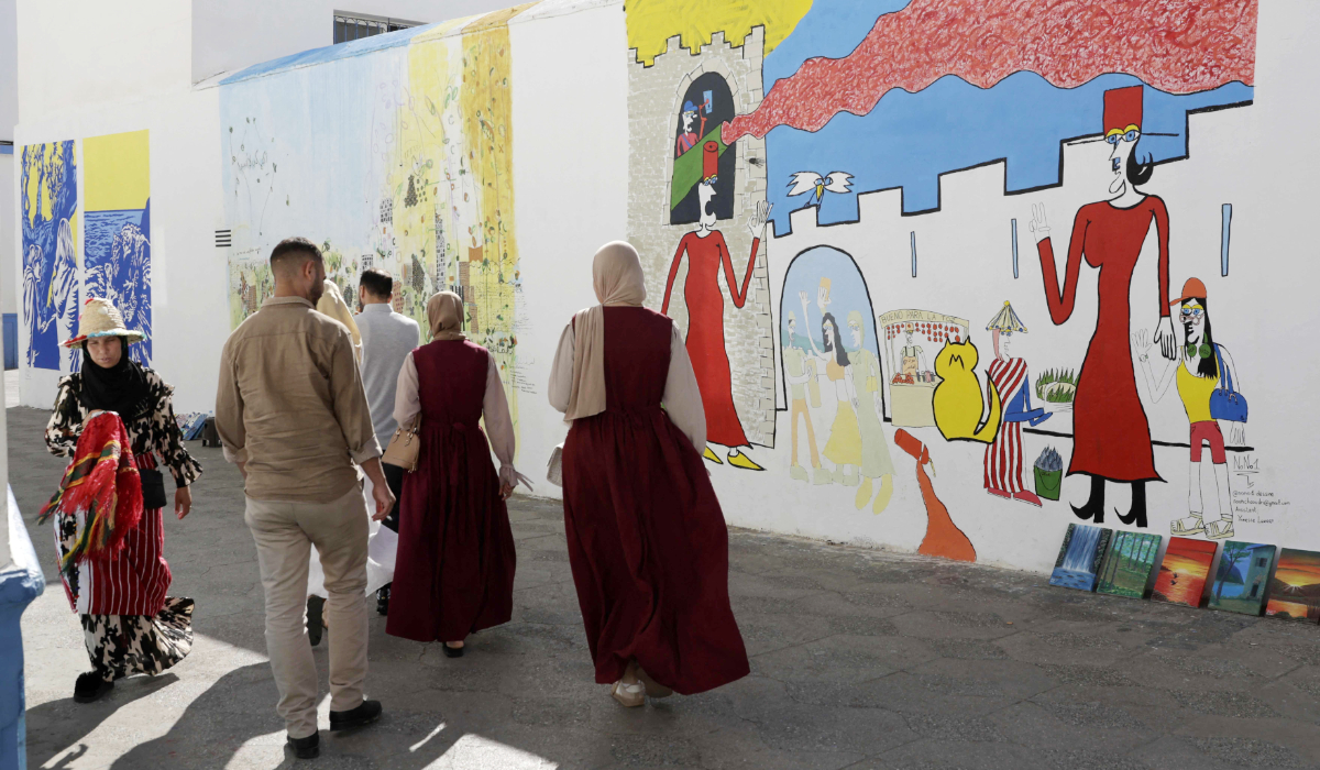 Visitors walk near mural paintings during the annual Asilah Arts Festival, which transforms the coastal Moroccan town into an open air art gallery, on July 12, 2025. (AFP)