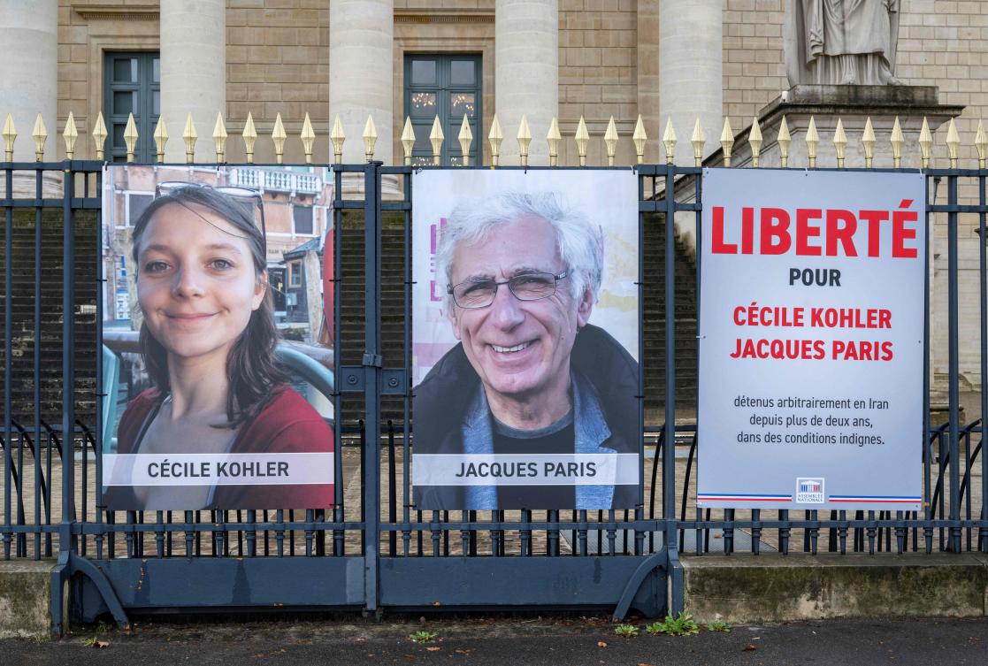 This photograph shows portrait placards of Cecile Kohler and Jacques Paris, two French citizens formerly detained in Iran, set up on a fence of the French National Assembly, in Paris on March 11, 2026. Former detainees Cecile Kohler and Jacques Paris “are free and on their way to France,” France’s President Emmanuel Macron announced on April 7, 2026. (AFP)