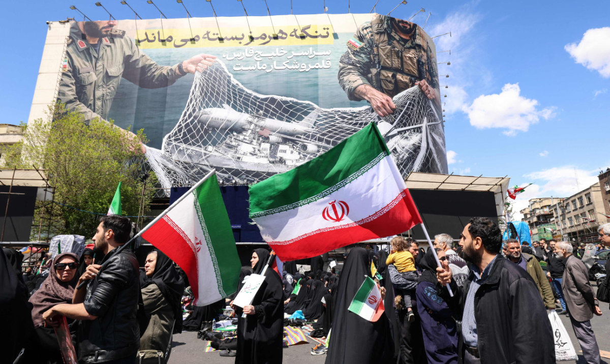 Iranians hold national flags beneath a large billboard reading "The Strait of Hormuz remains closed" as people gather in Tehran's Revolution Square after the United States and Iran agreed to a two-week ceasefire, on April 8, 2026. (AFP)