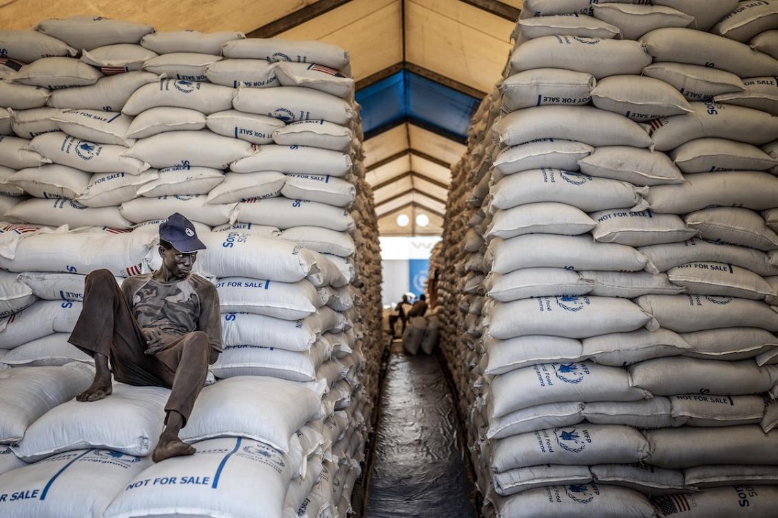 A worker sits atop sacks of food aid in a hangar where supplies are piling up because deliveries are halted due to insecurity from the conflict, at a World Food Programme (WFP) warehouse in Bor, Jonglei State, on February 13, 2026. (FILE/AFP)