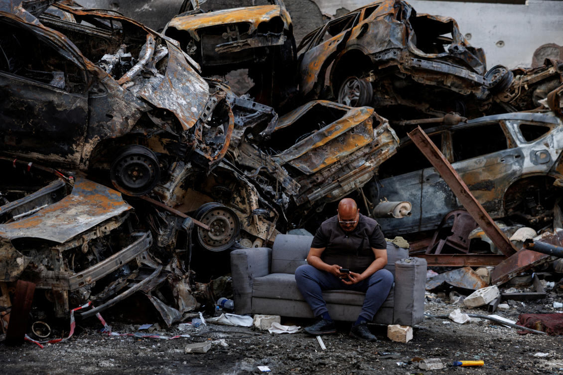 Mohamed Al-Junayd, 43, who survived an Israeli strike last week in Beirut, sits beside piled damaged cars at the site on Monday. (Reuters)